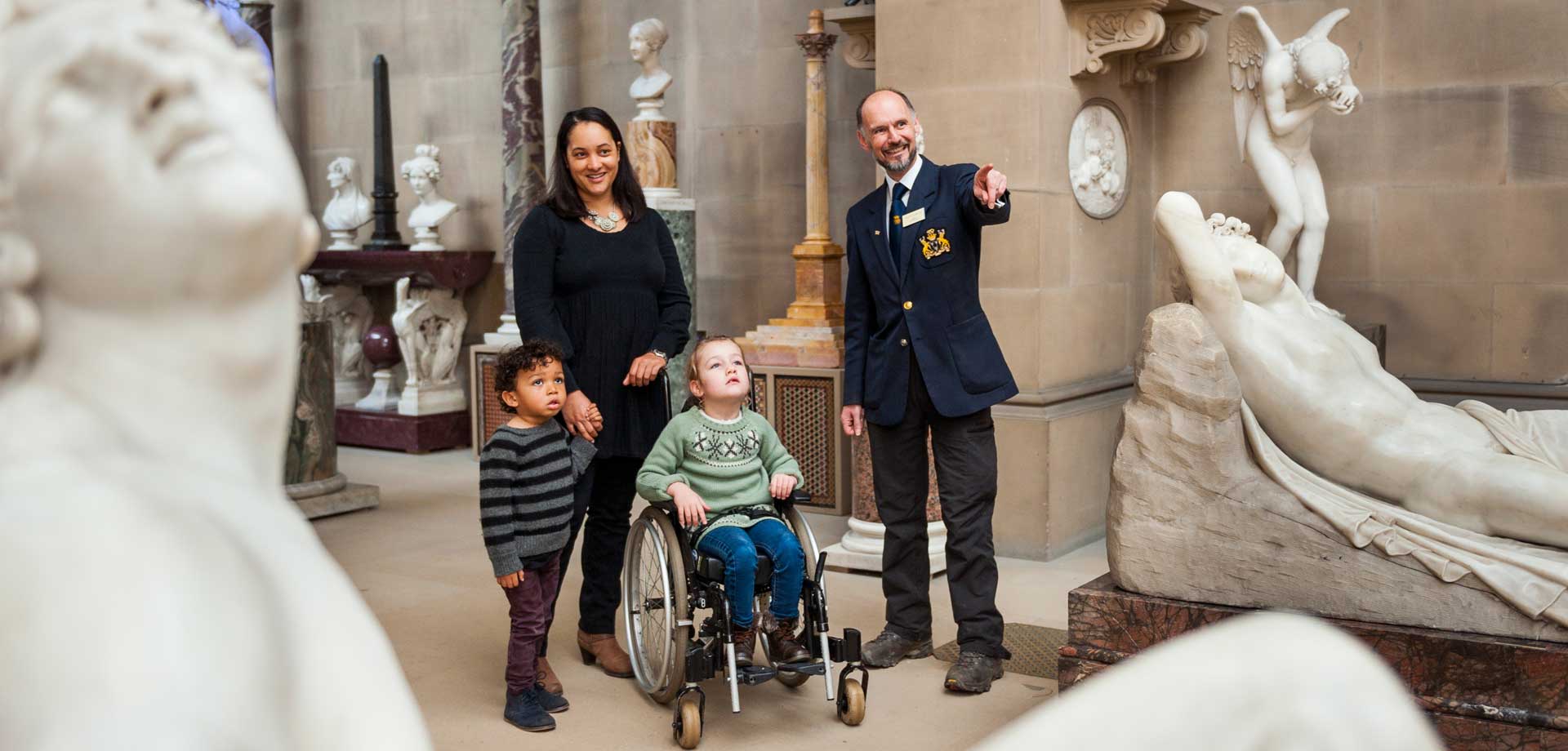 A wheelchair user visiting the Sculpture Gallery at Chatsworth with family and a member of staff