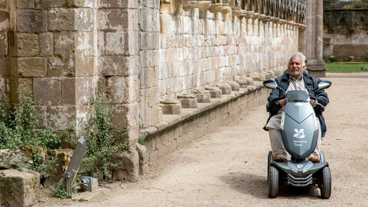 A visitor using a National Trust mobility scooter on a level route beside Fountains Abbey ruins