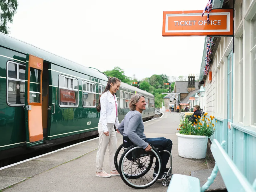 A wheelchair user beside a heritage train at Grosmont station