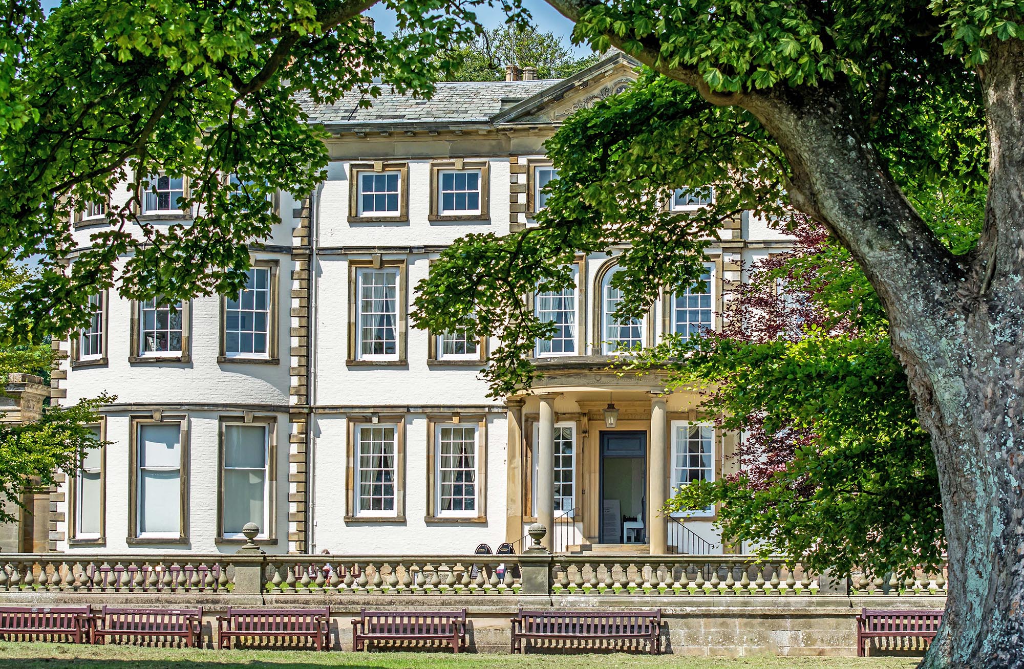 Sewerby Hall framed by trees with benches across the lawn