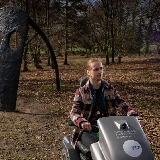 A visitor using an off-road mobility scooter beside a sculpture at Yorkshire Sculpture Park